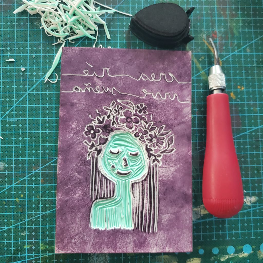 block print of a woman's portrait with flowers in her hair. Carving tool is displayed and ink pad as well